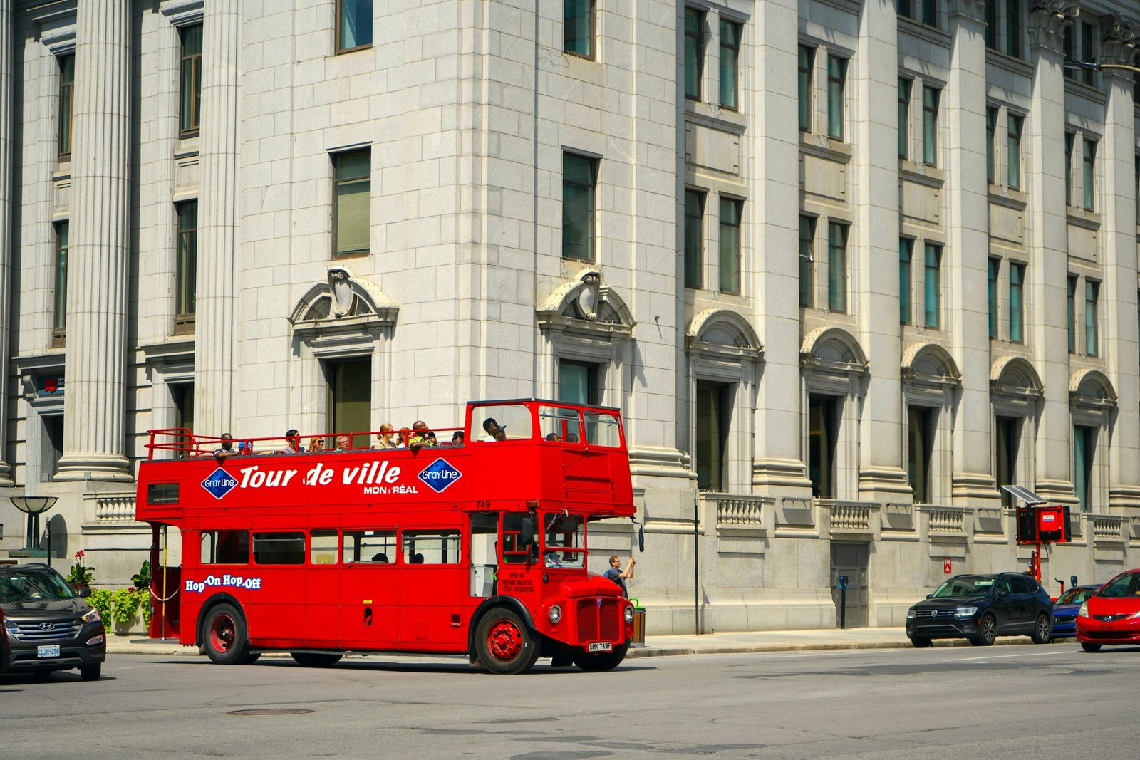 Red double-decker tour bus on city street in Montreal, Canada with historic architecture.